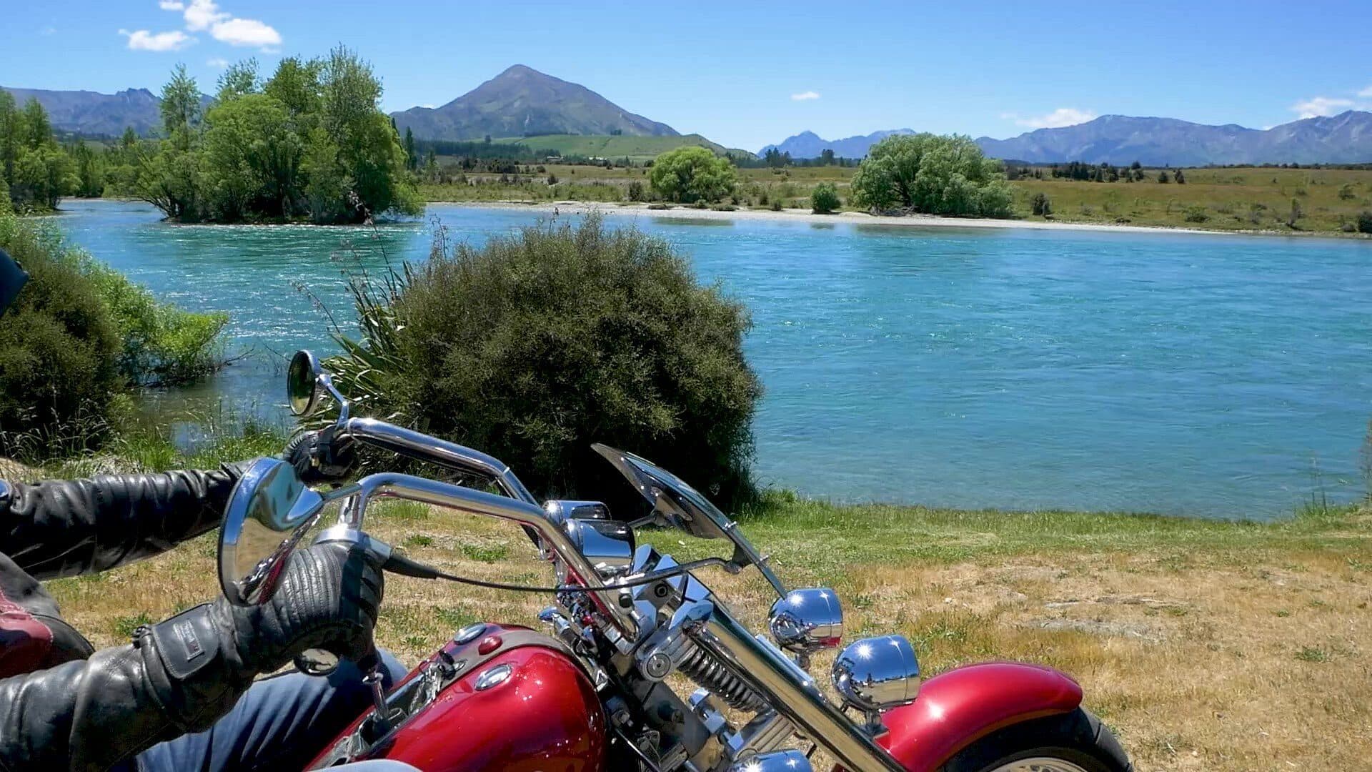 Trike handlebars and red front wheel with Lake Wānaka and mountains behind