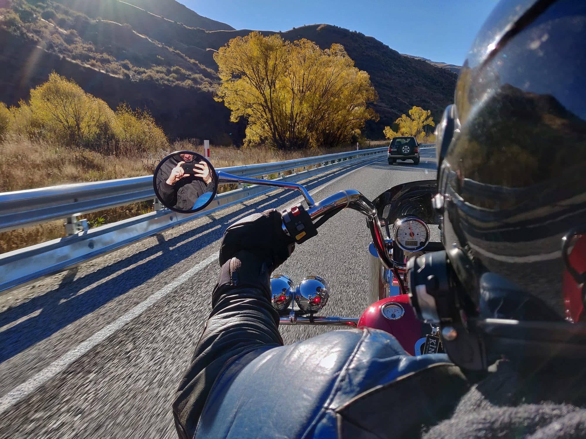 Rider's view from a trike on a highway lined with autumn trees and mountains
