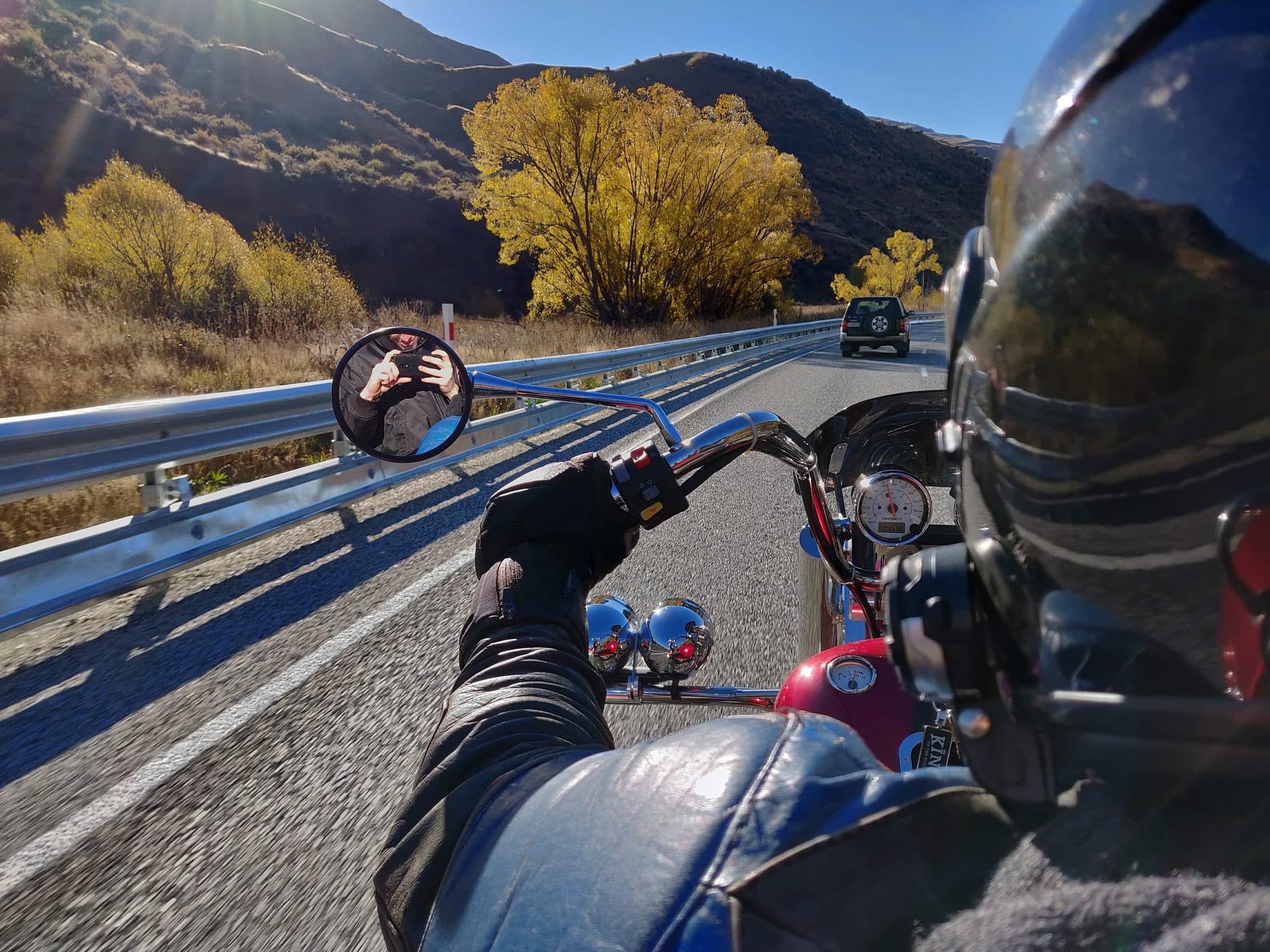 Rider's view from a trike on a highway lined with autumn trees and mountains