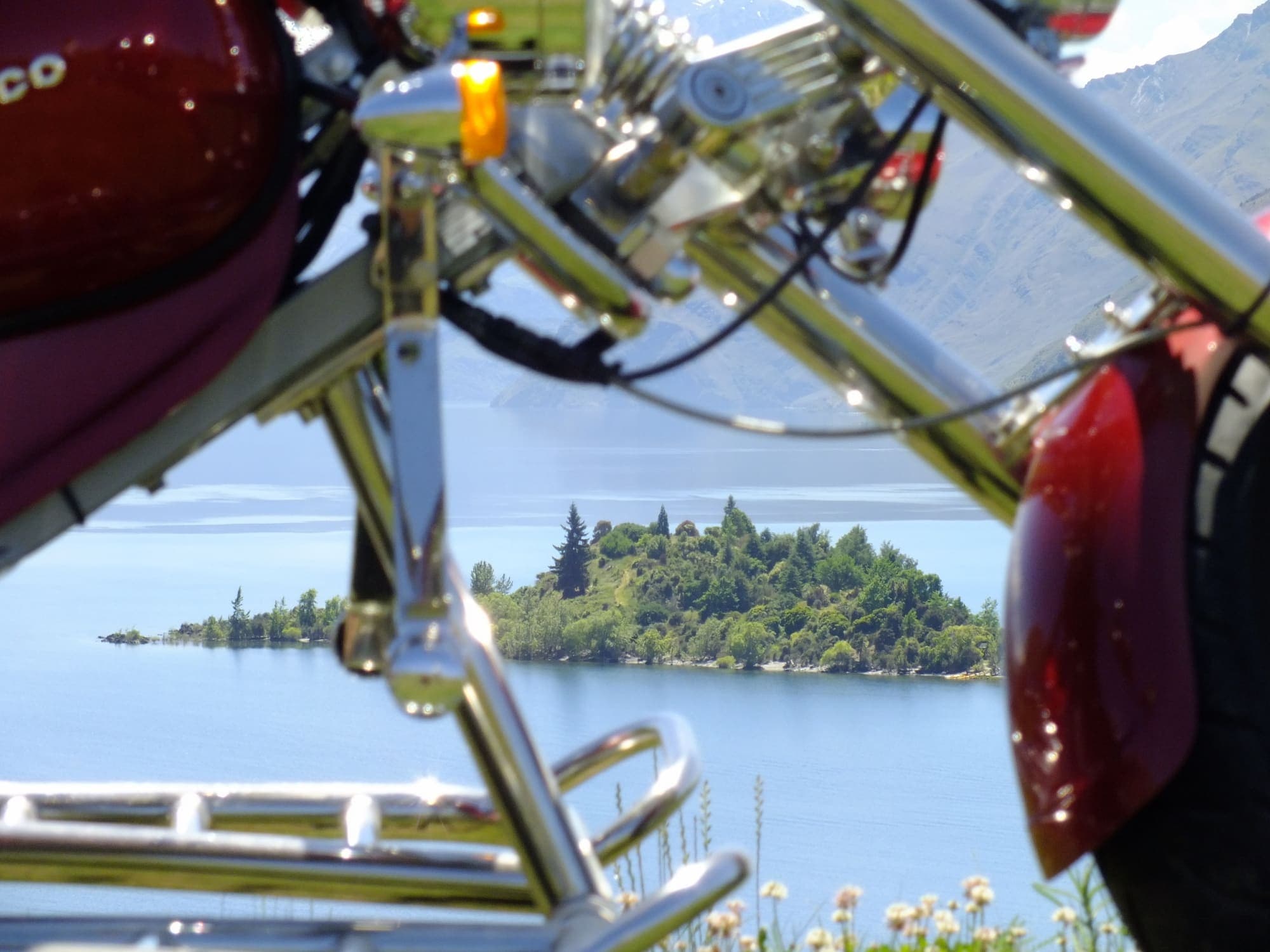 Red trike parked beside Lake Wānaka with mountains behind