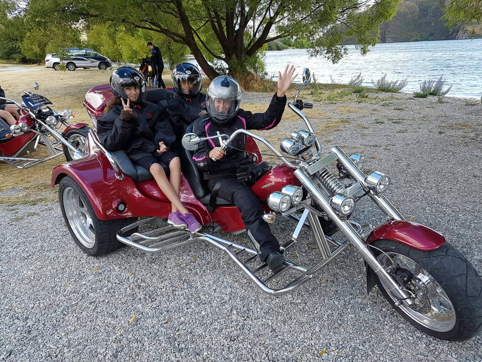 Two red trikes with guests in helmets at a lakeside gravel stop
